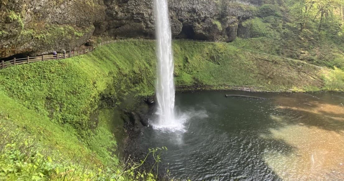 Waterfall plunging into green pool at riverside trail