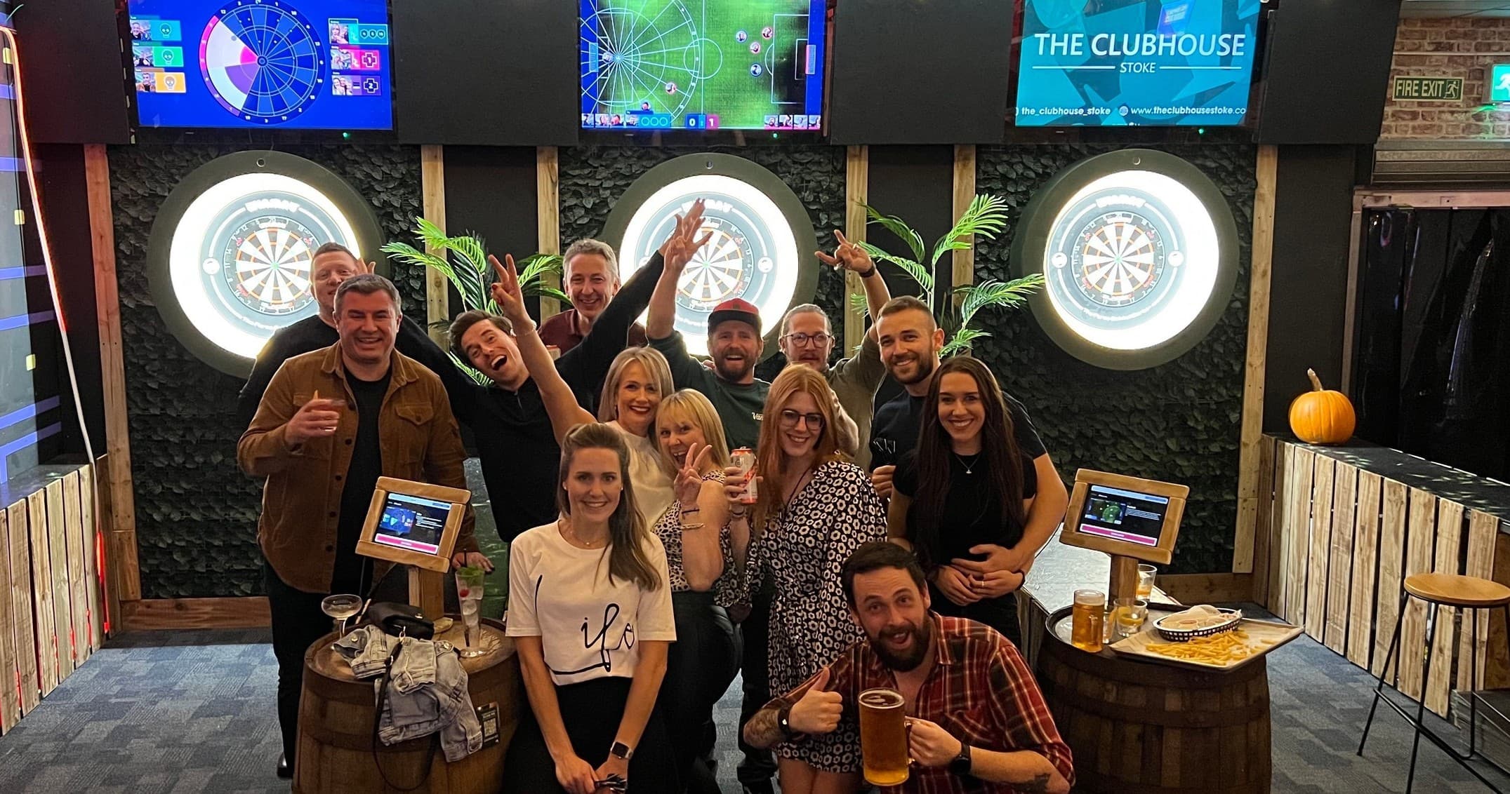 Group posing by dartboards and screens at indoor leisure venue