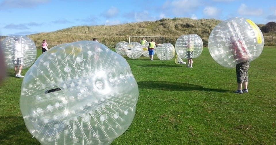Players in zorb balls rolling across open grassy hillside field