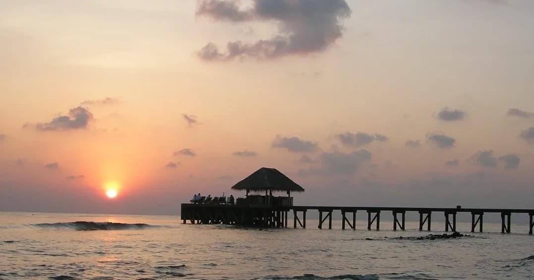 Sunset over ocean pier at tropical beach, serene seaside view