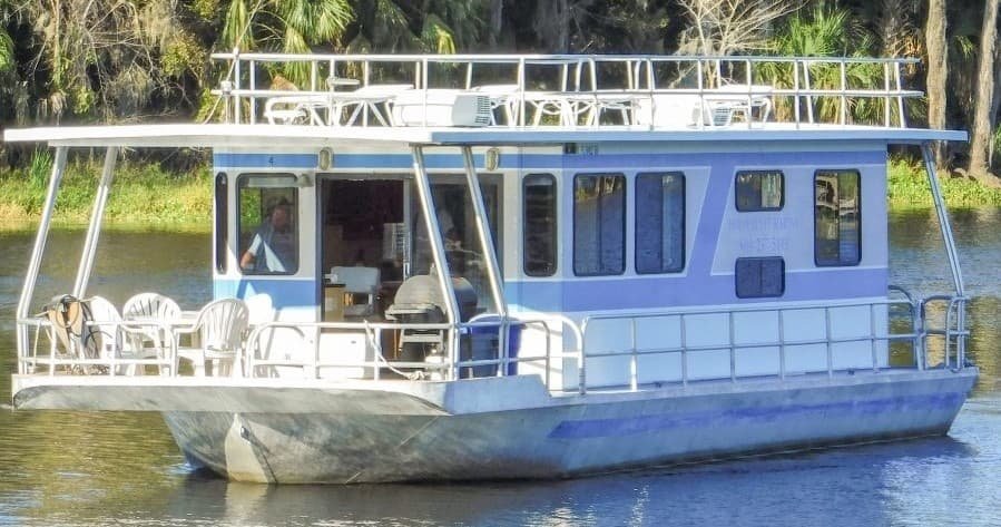 Blue-and-white houseboat gliding on scenic lake near trees
