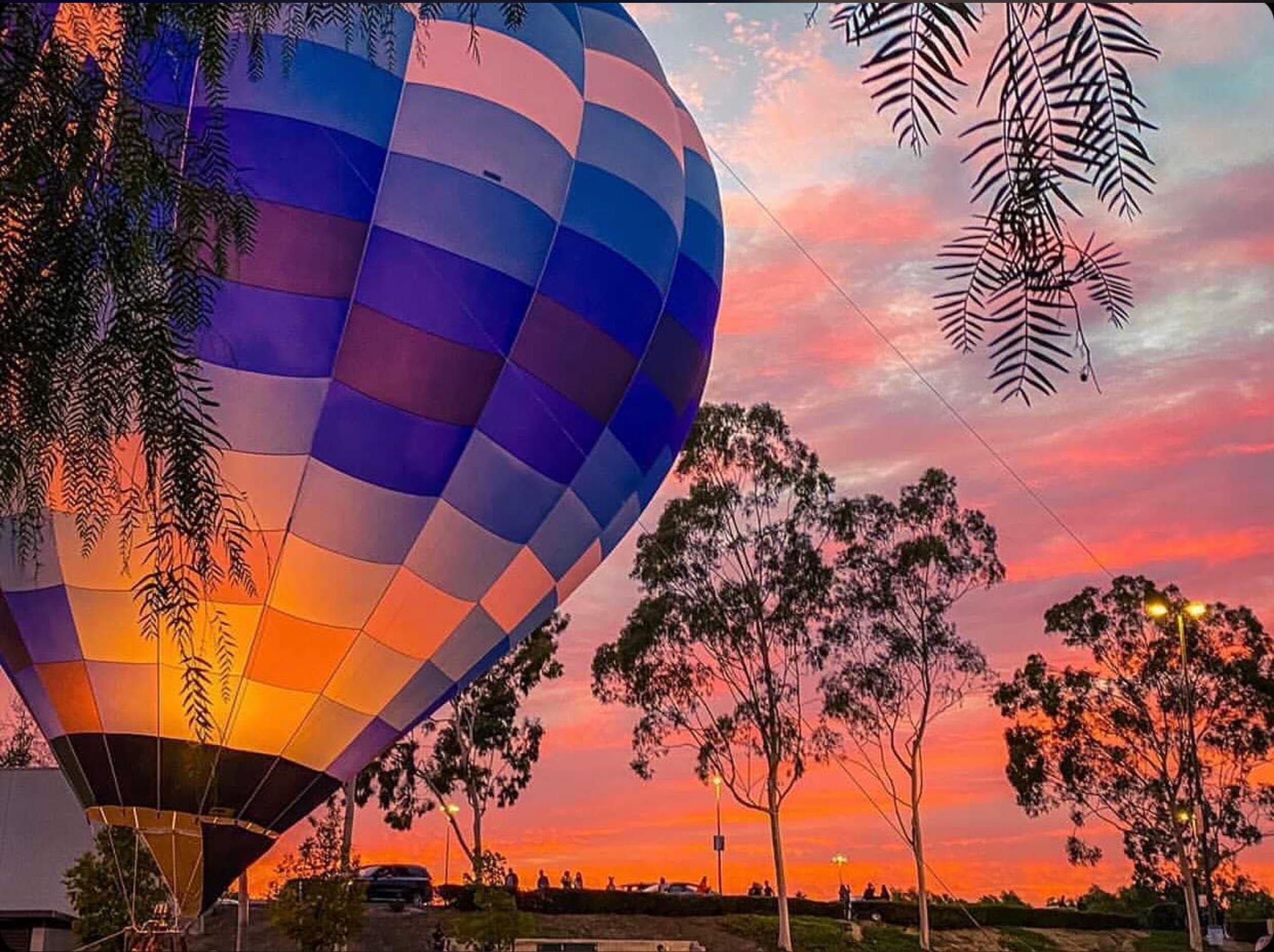 Hot air balloon glowing at sunset over rural countryside