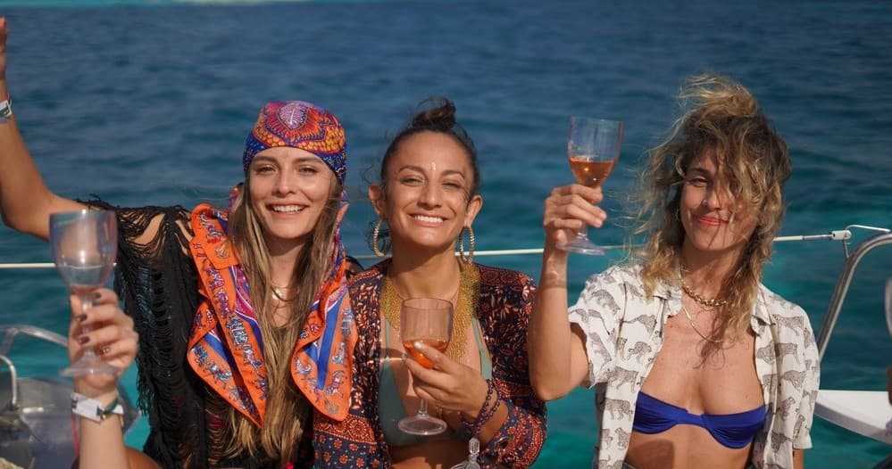 Friends toasting drinks on deck of sailboat, coastal cruising vibe