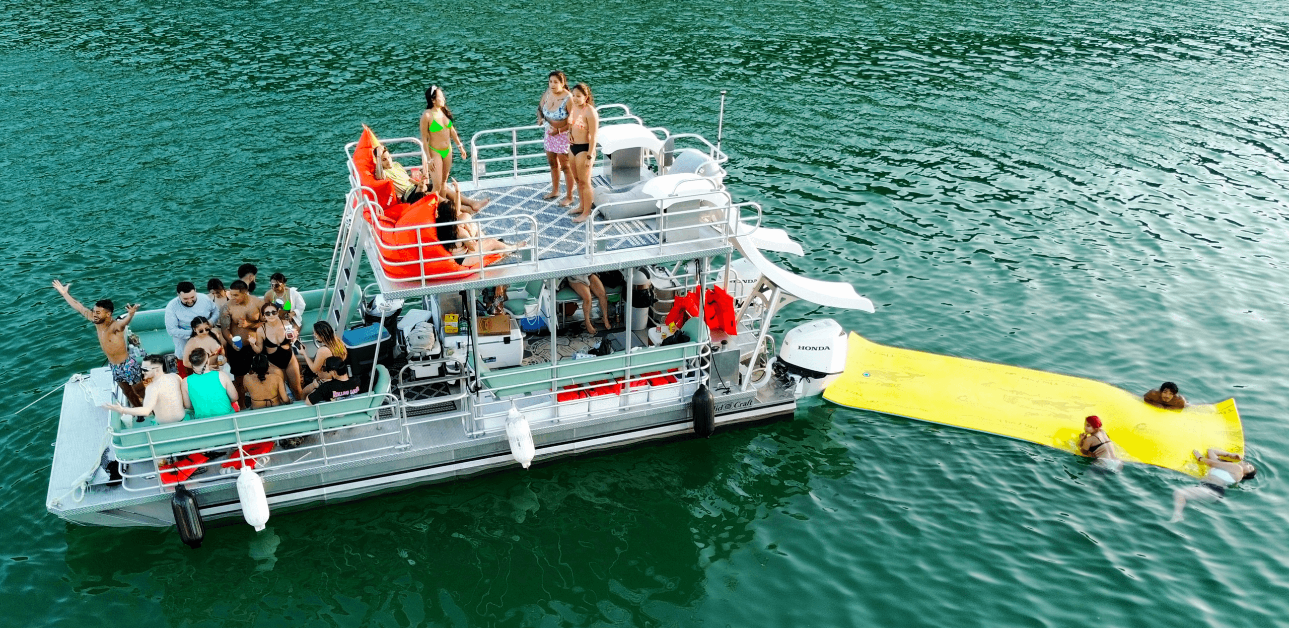 Crowded party pontoon with slide and swimmers on lake