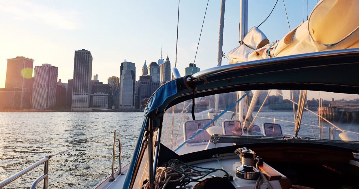 Sailboat bow facing New York City skyline at sunset