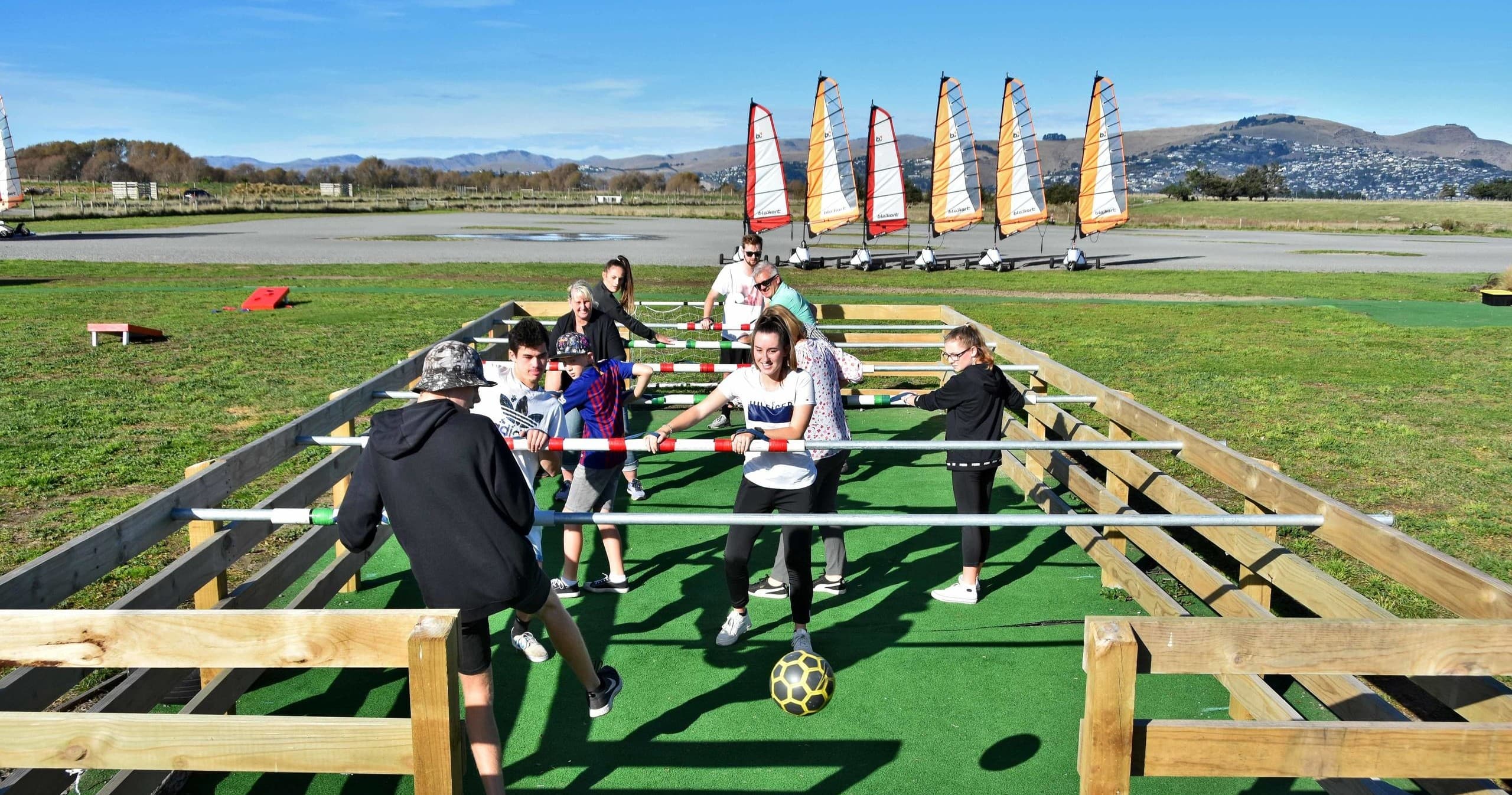 Outdoor human foosball game on turf with sailboats in distance