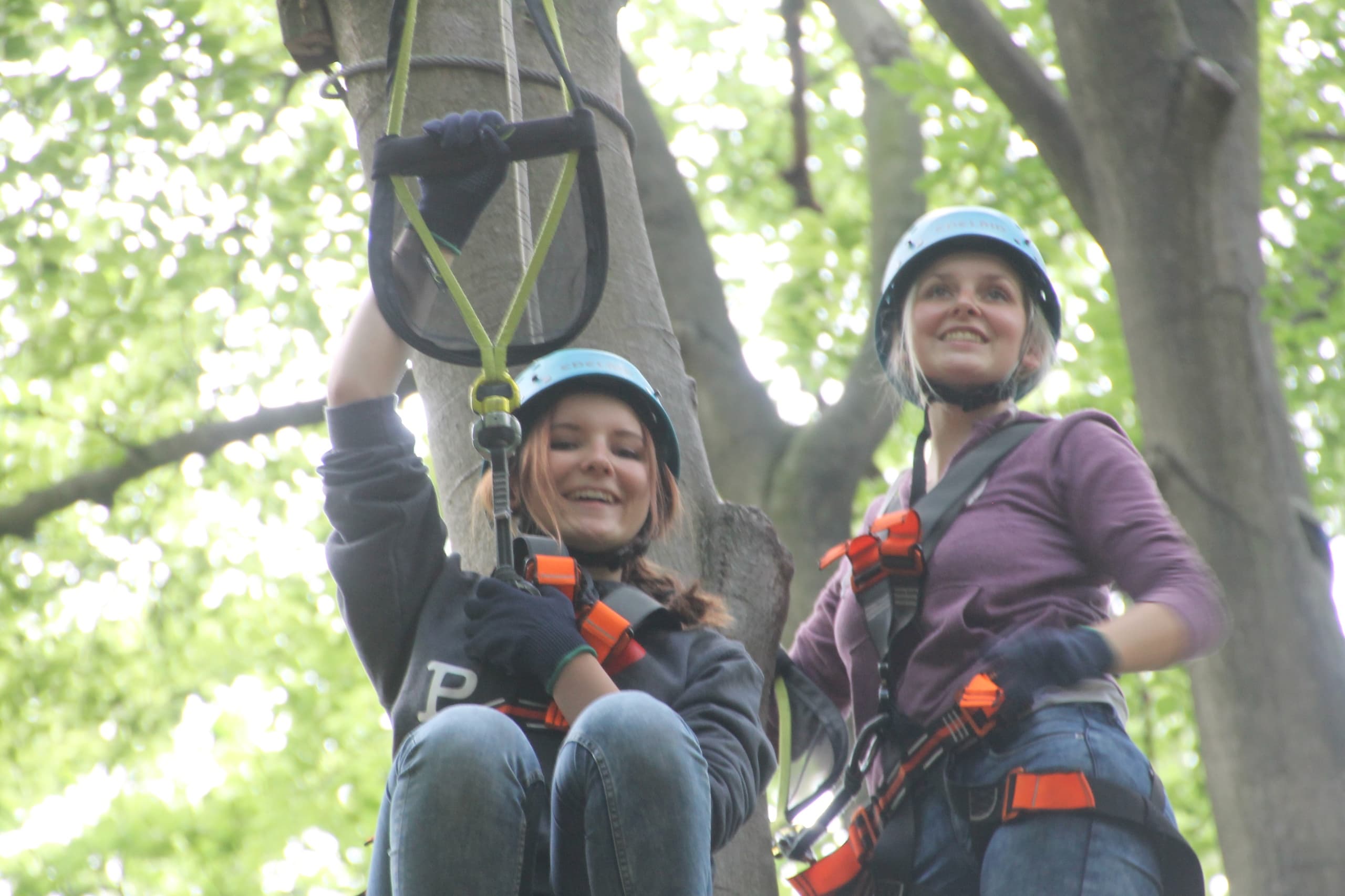 Two participants smiling in harnesses on treetop zipline course