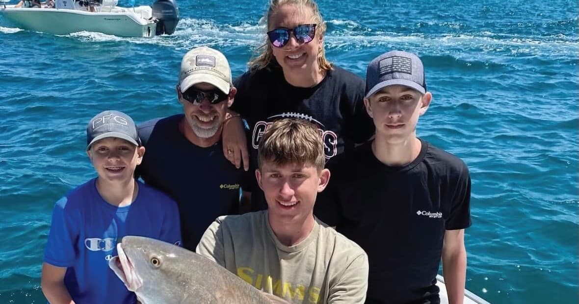 Family group aboard boat holding a caught fish in open sea