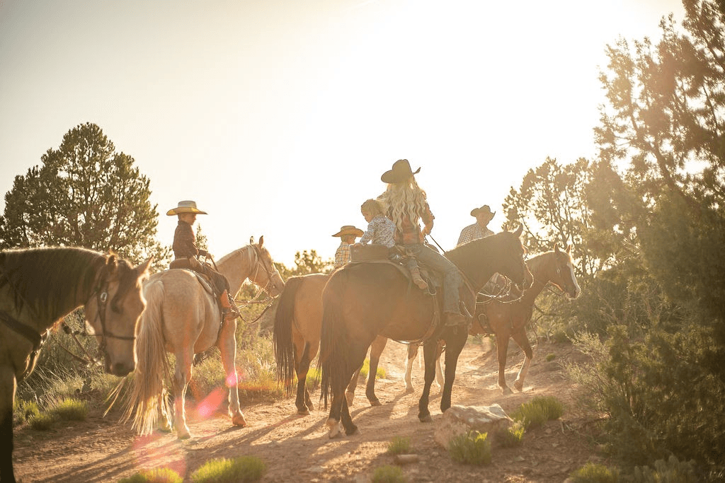 Group horseback trail ride backlit by golden sunset in scrubland