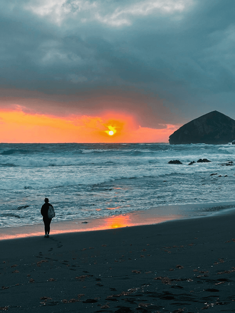 Solitary walker on Azores beach at dramatic sunset over ocean