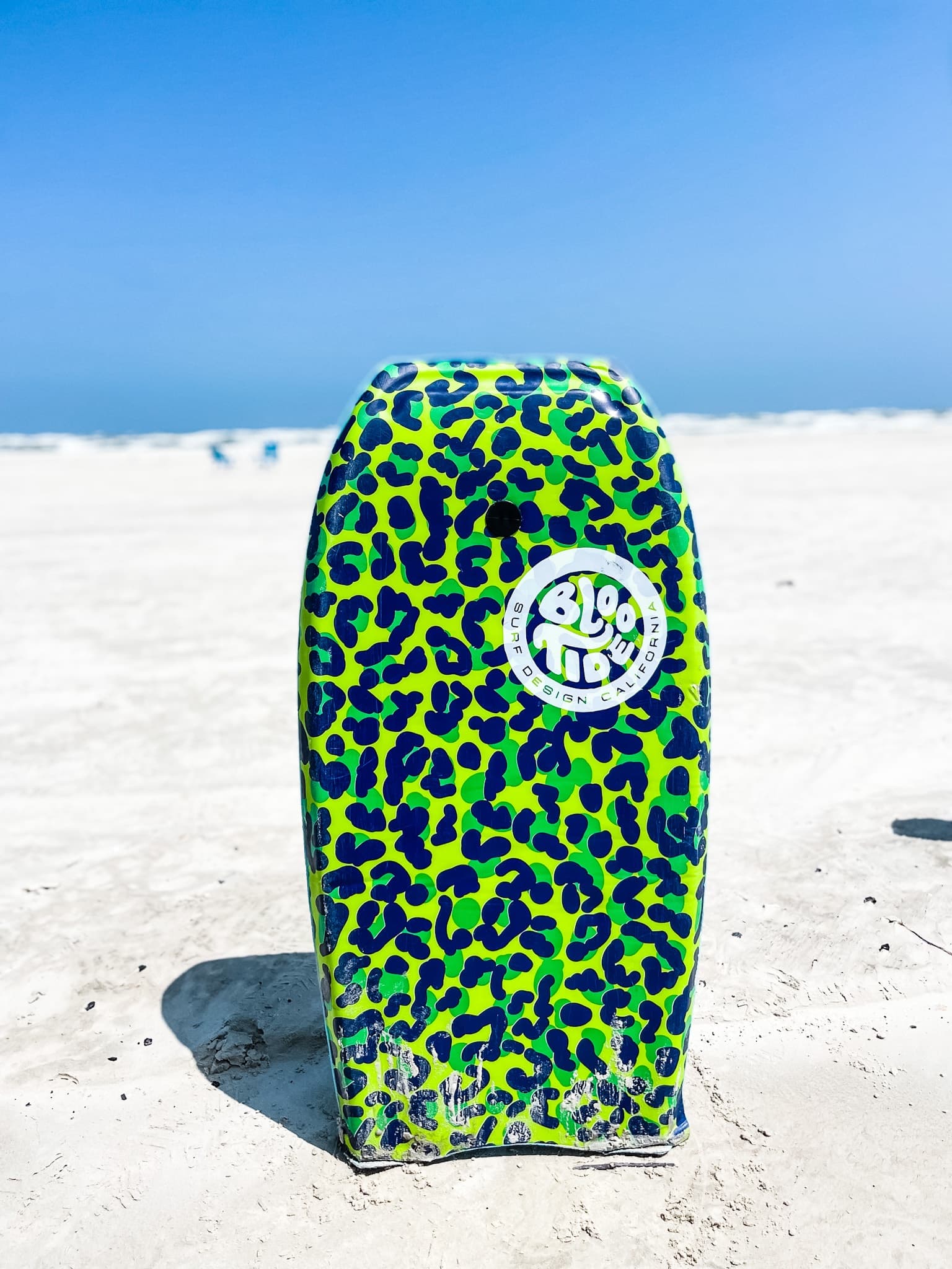 Leopard-print bodyboard standing upright on sunny sandy beach