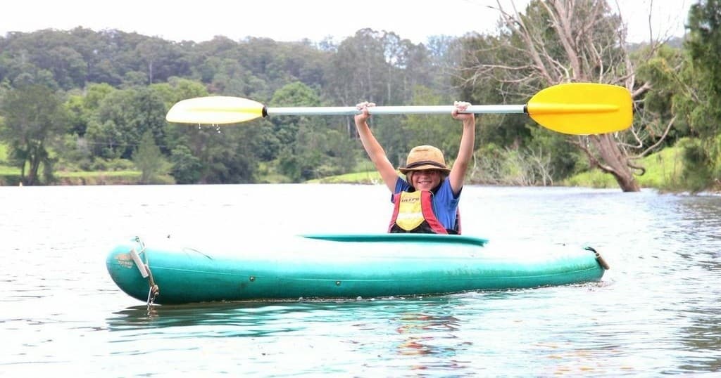 Solo kayaker cheering with paddle on tranquil lake shore