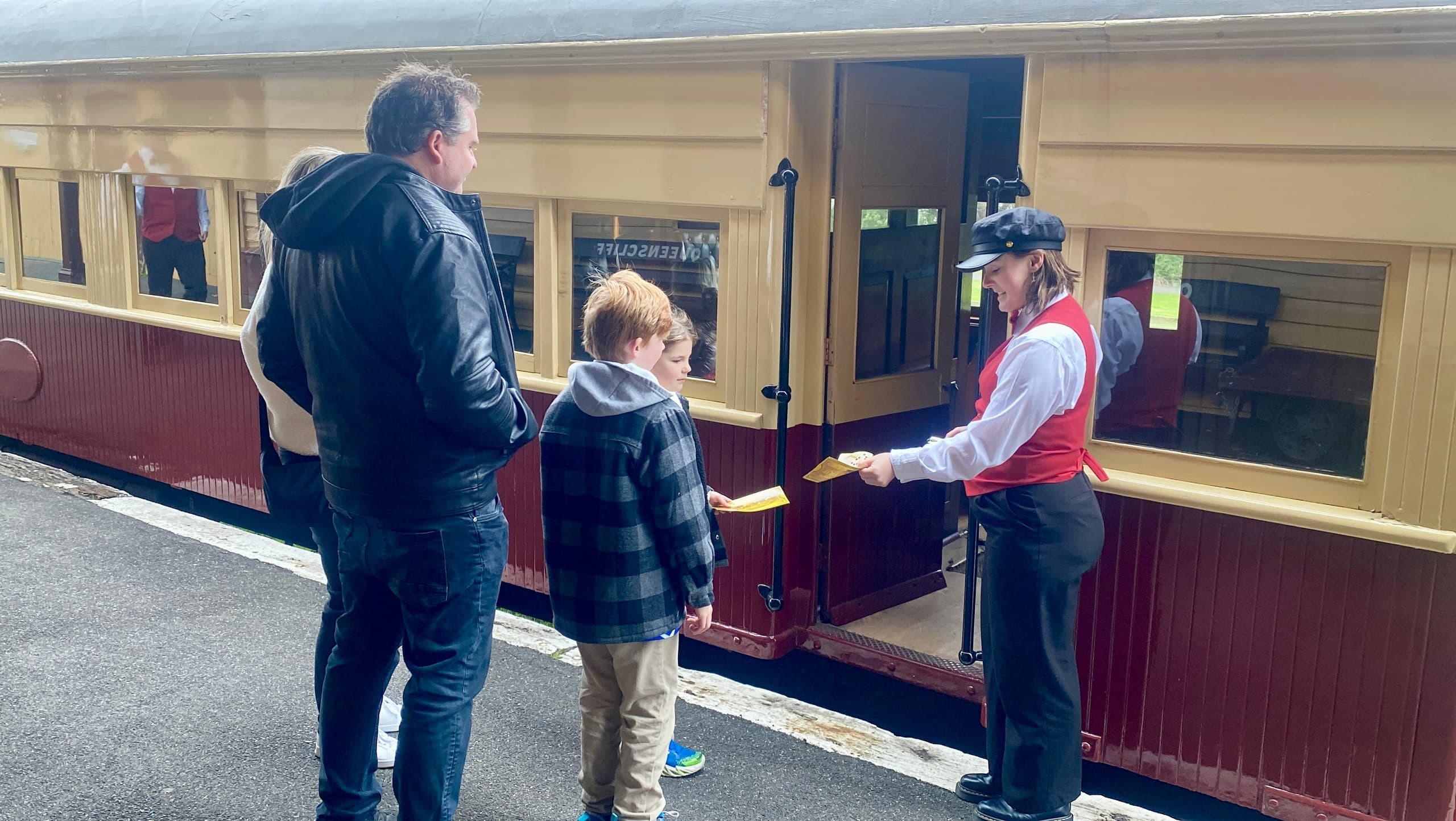 Conductor handing tickets to family beside vintage passenger carriage