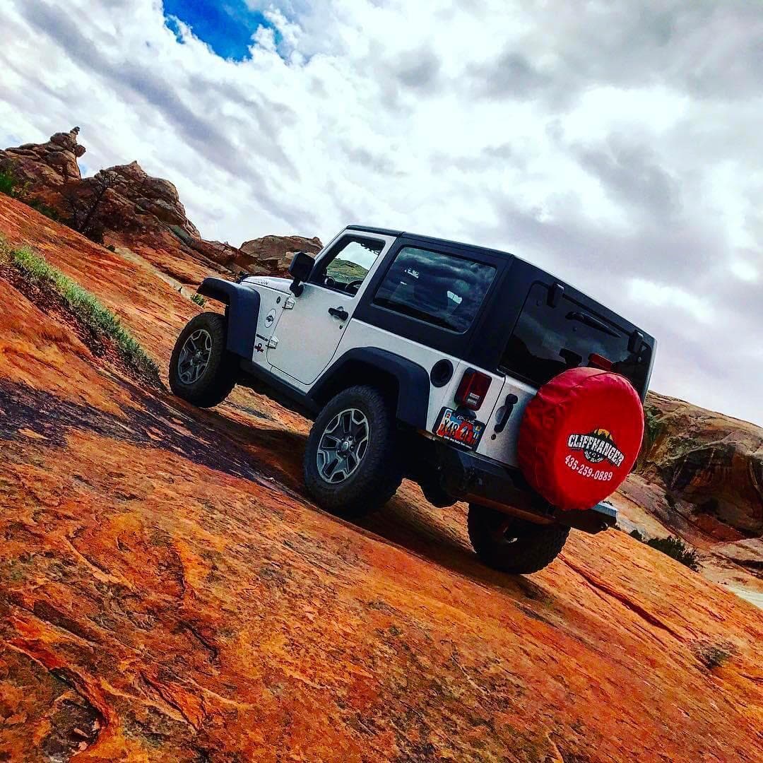White Jeep climbing tilted red slickrock for scenic off-road drive