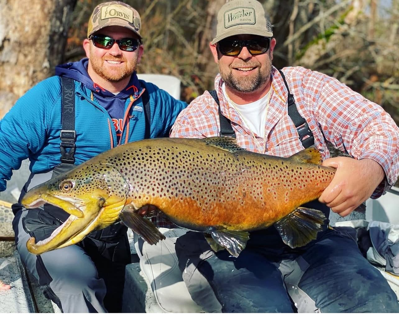 Two anglers holding massive brown trout on guided fishing charters