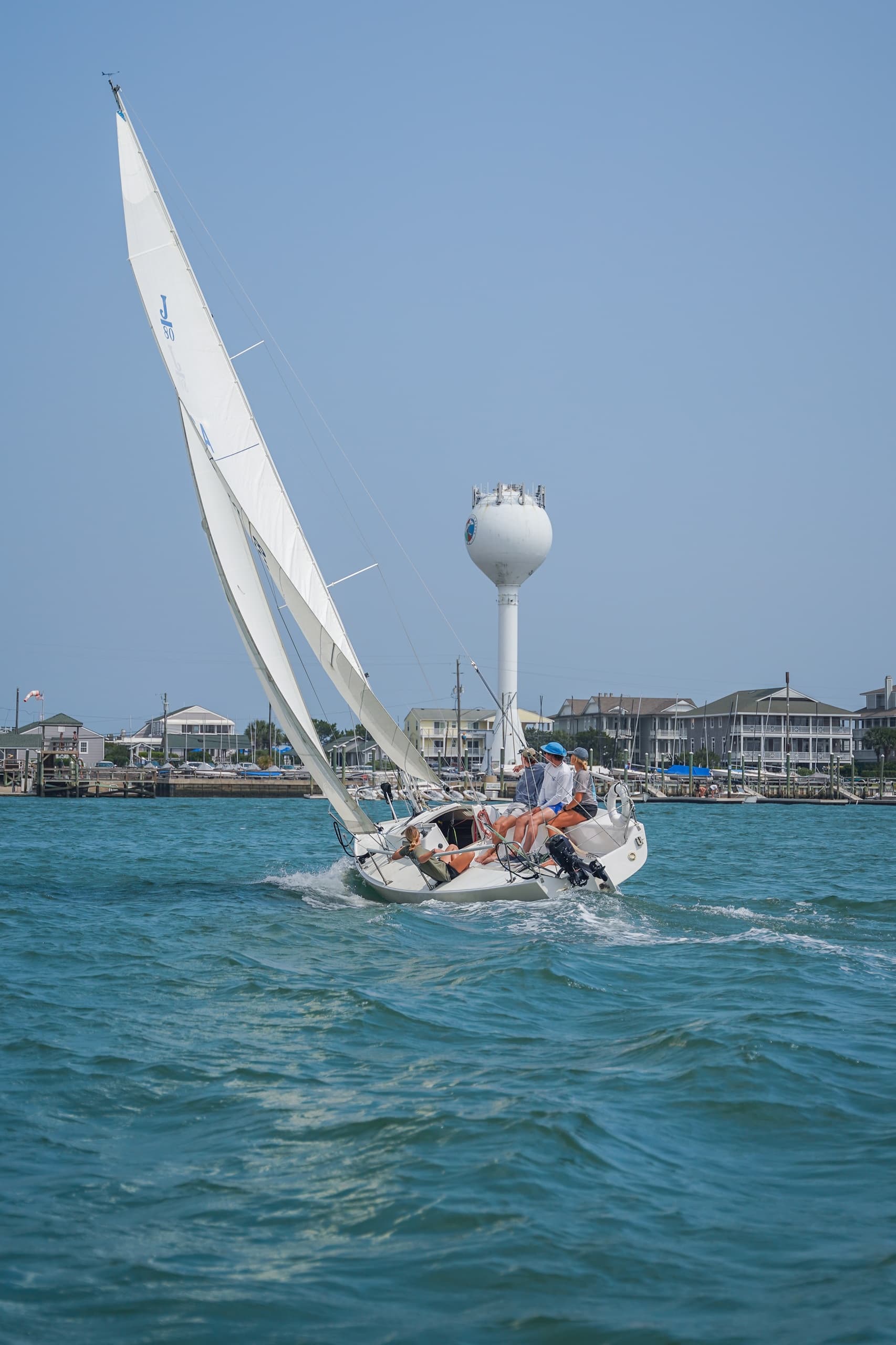 Sailboat racing past coastal waterfront with distant water tower