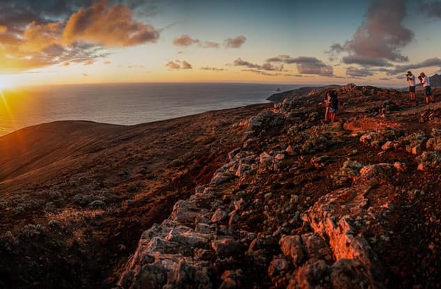 Sunset cliffside vista with off-road vehicles and coastal hikers