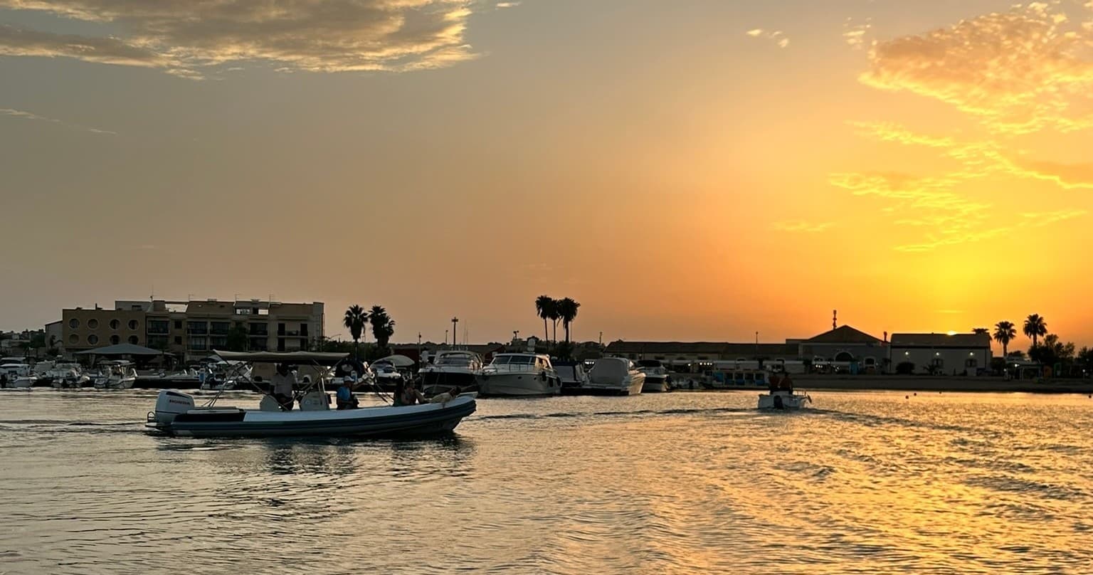 Calm Sicilian harbor at golden hour with moored tour boats
