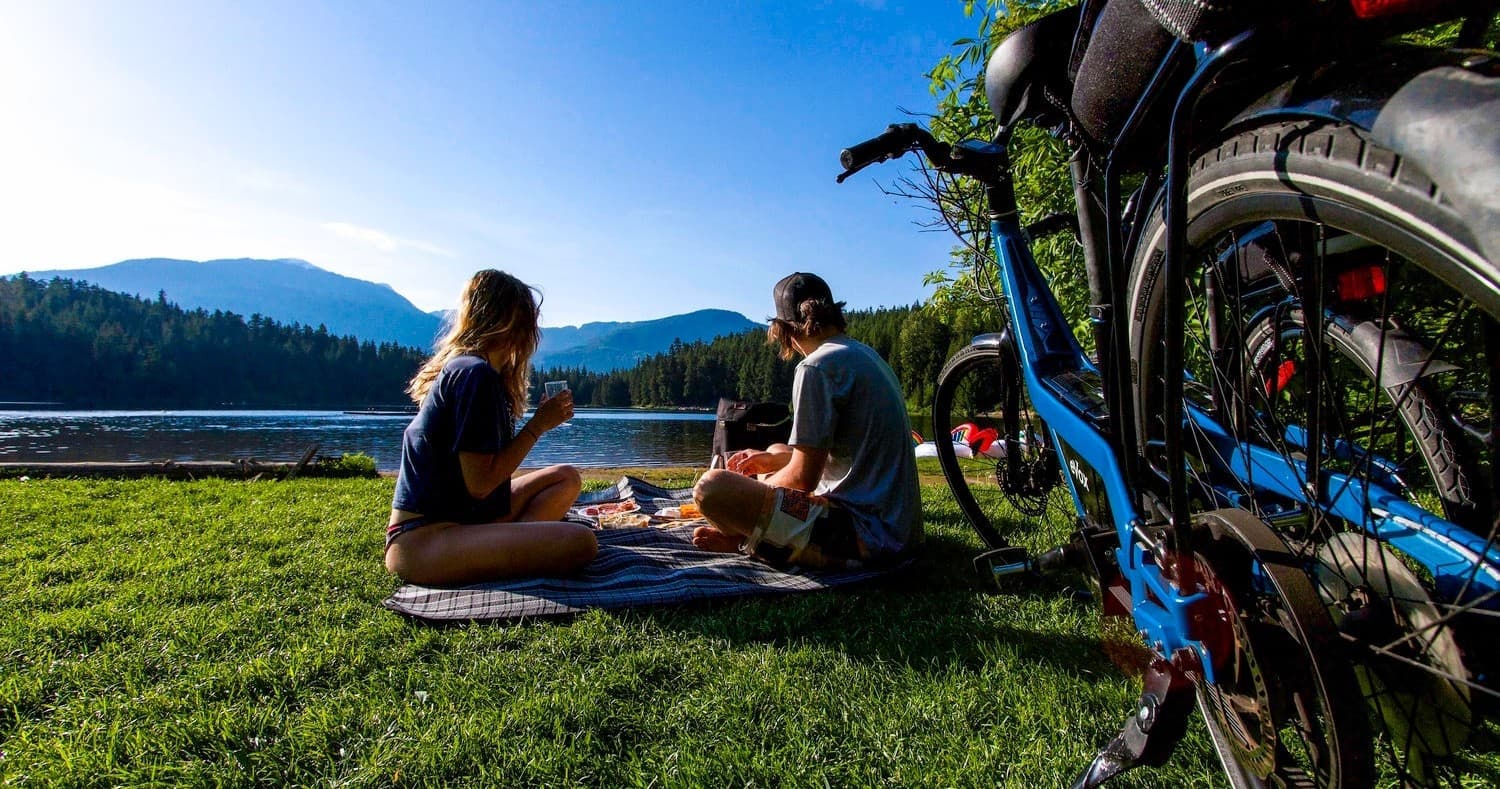 Couple picnicking by bikes on grassy lake shore with mountains