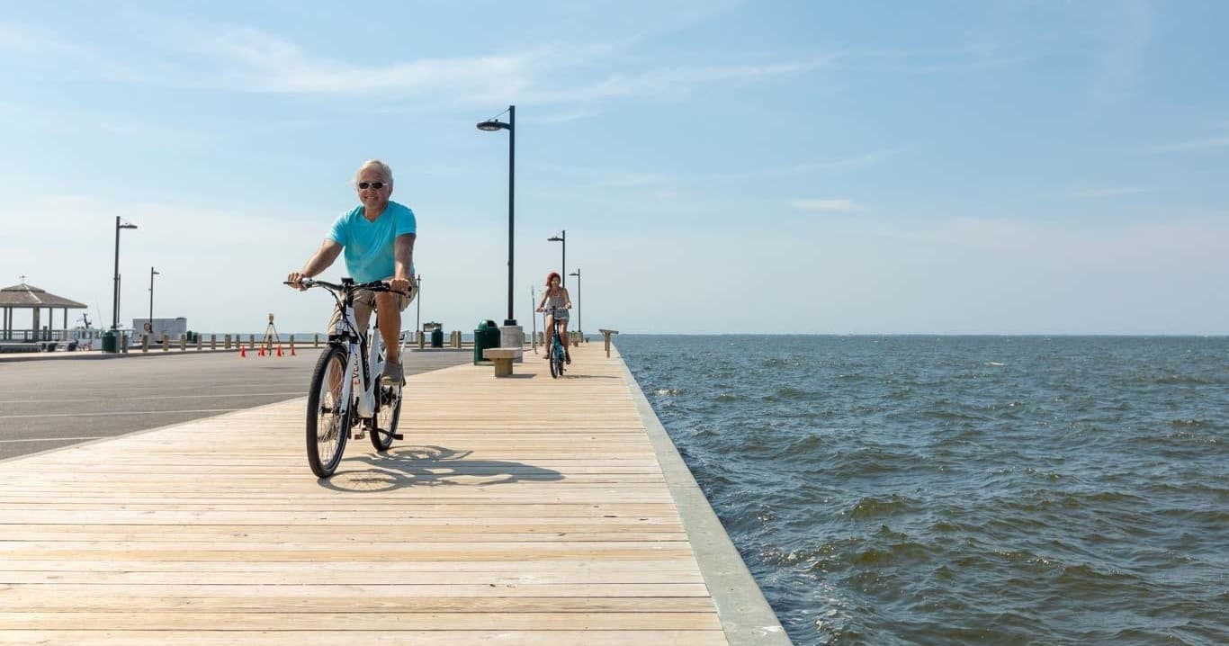 Cyclist riding on ocean boardwalk with pier and clear sky