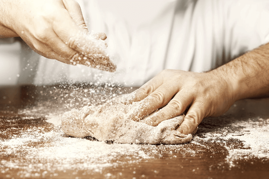 Chef kneading dough on floured wooden counter in kitchen