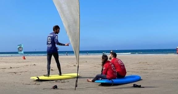 Surf instructor coaching students on beach with boards and sail