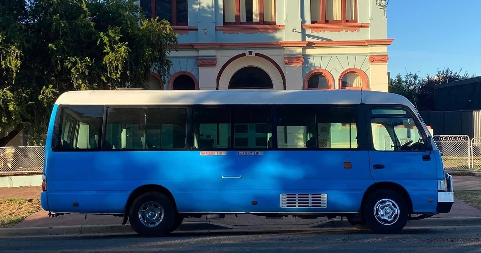 Tour minibus parked near ornate building and leafy street scene