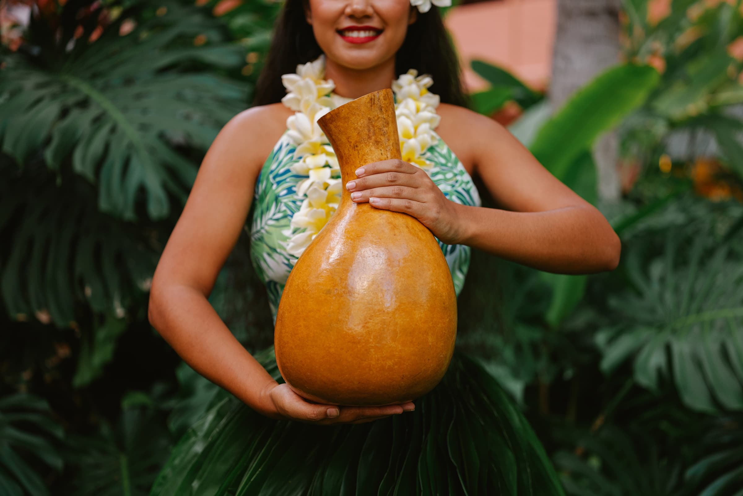 Female hula performer holding traditional gourd in lush foliage