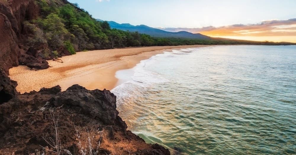 Sunset coastal bay with rugged cliffs and sandy beach in Hawaii