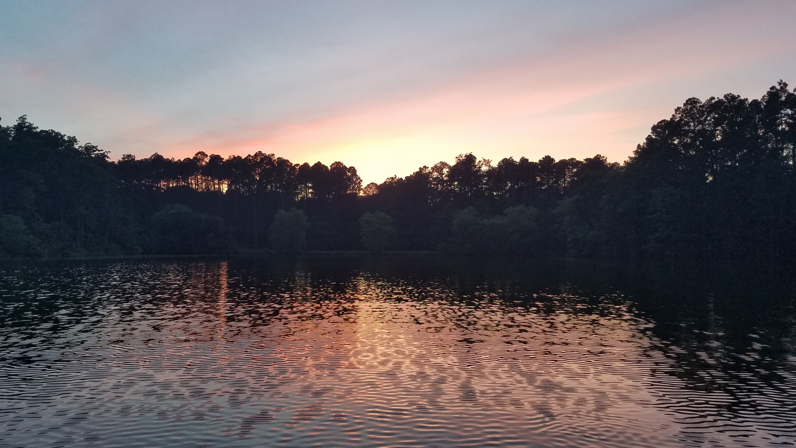 Sunset over a tree-lined lake with warm orange reflections