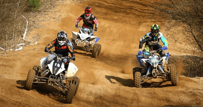 Four ATVs racing on dusty dirt track, competitive off-road race action