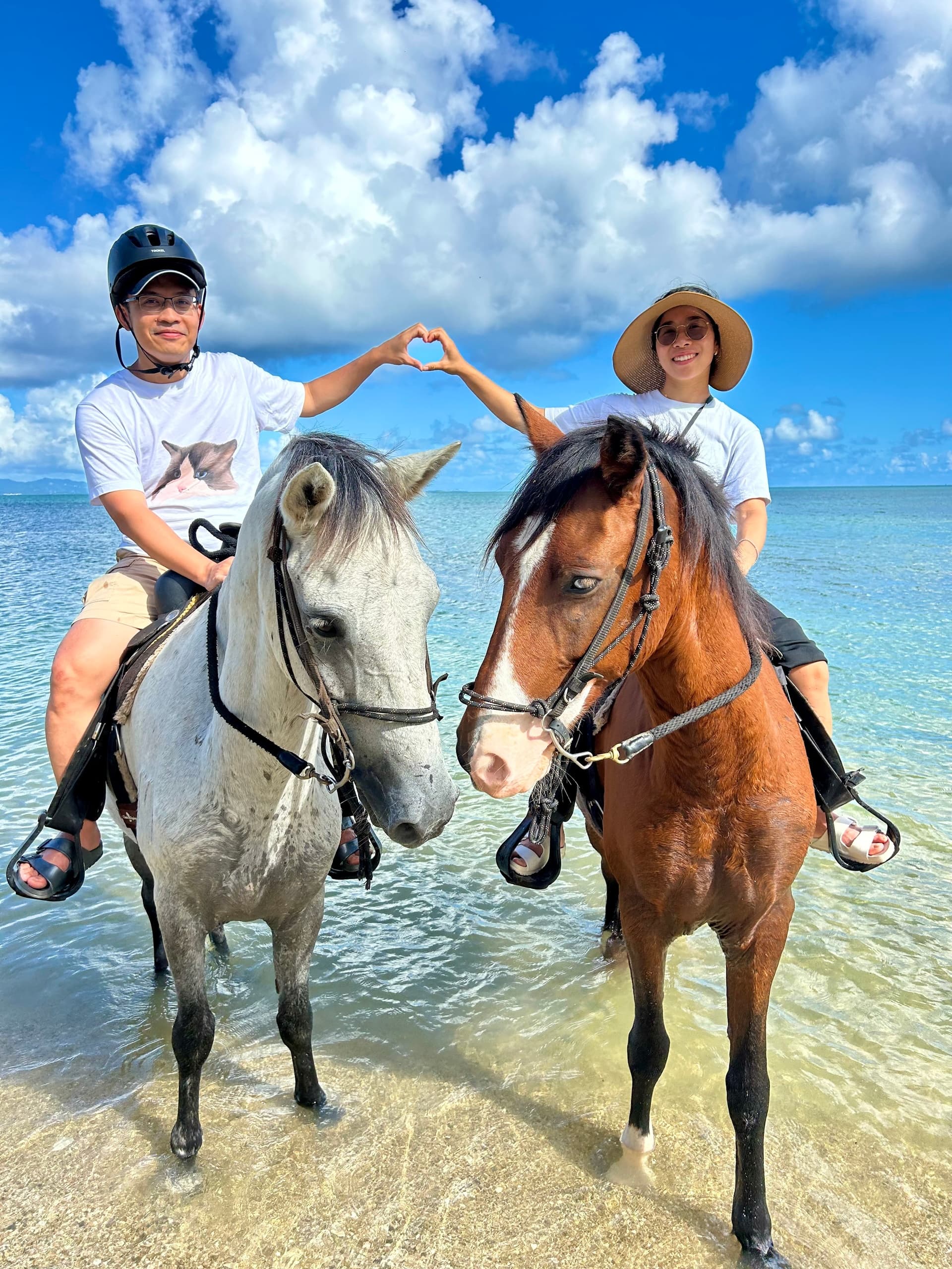 Two riders on horses forming heart gesture in turquoise sea