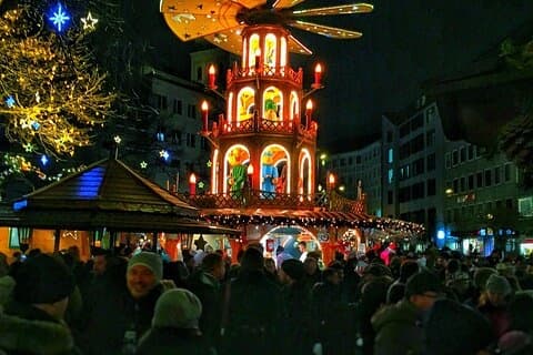 Outdoor Christmas market at night with illuminated pyramid and crowd