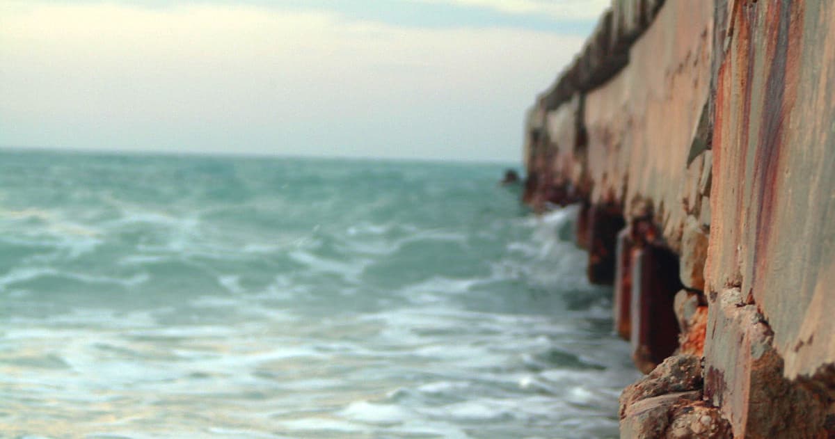 Waves crashing against rusted beachfront pier at low tide