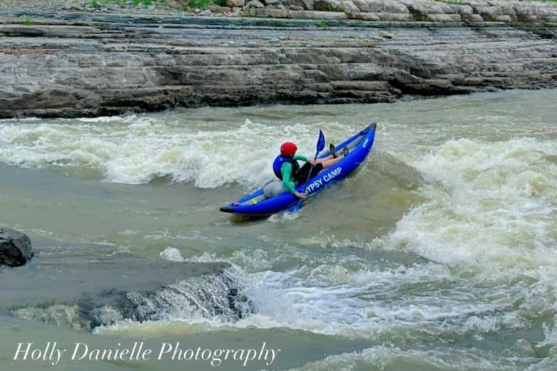 Solo kayaker dropping into turbulent whitewater below cliffs