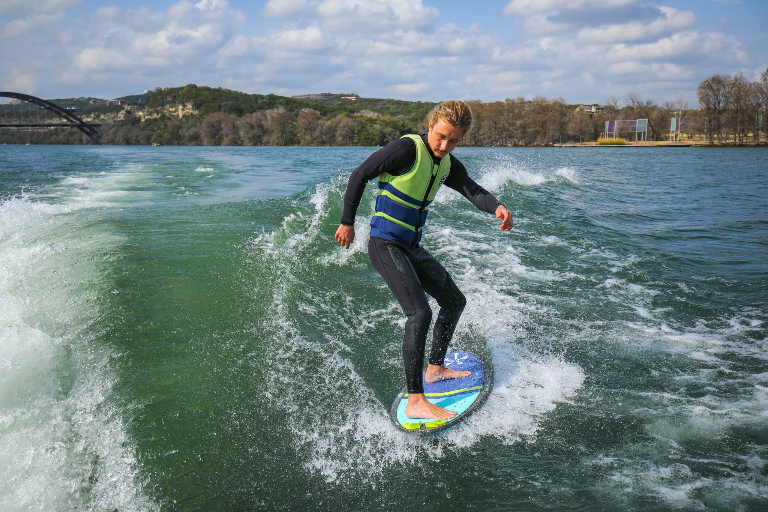 Wakesurfer carving wake behind boat on Lake Austin, sunny action