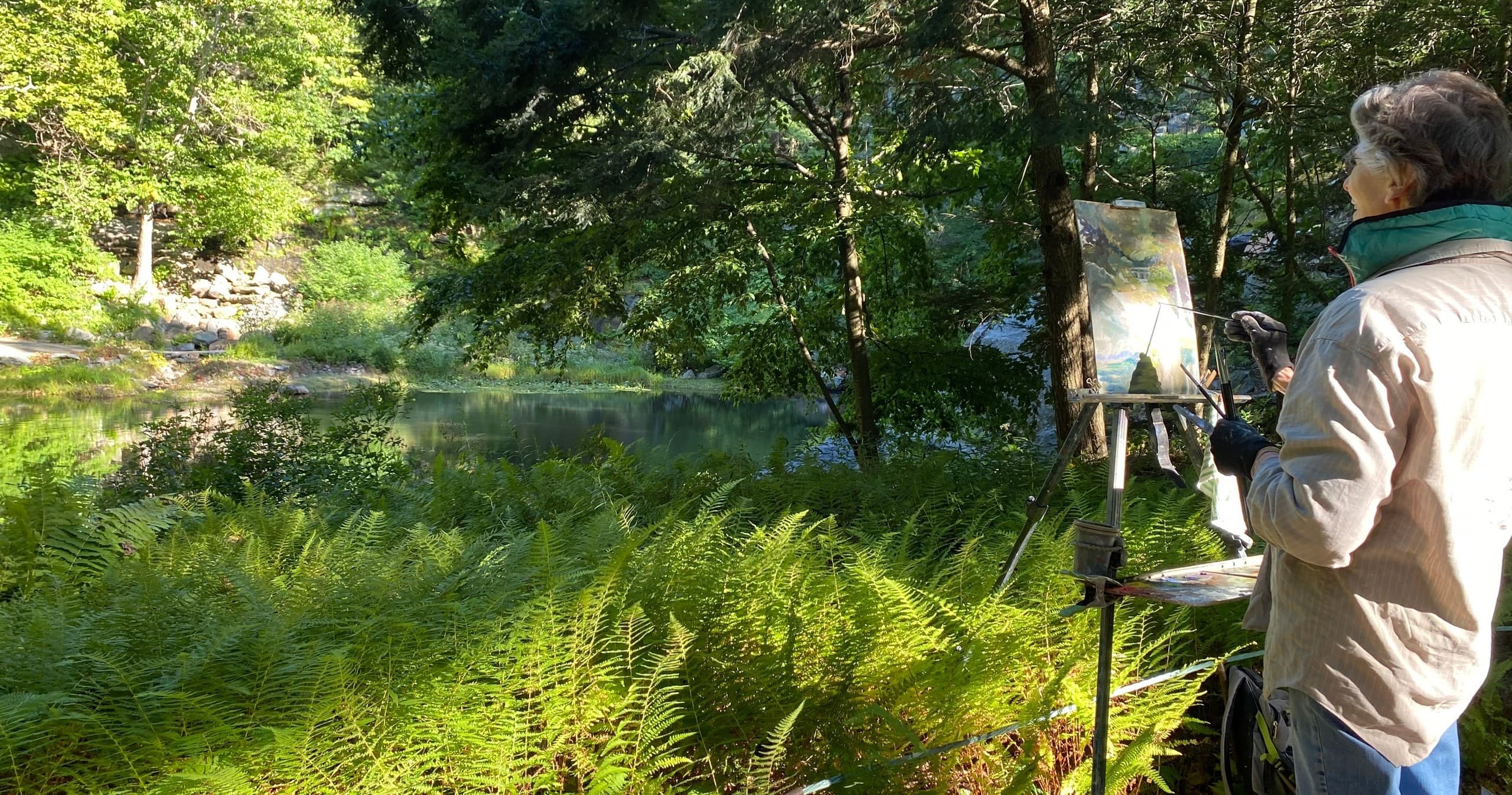 Artist painting plein air beside fern-filled woodland pond at Manitoga