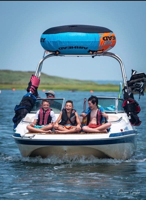 Group riding bow of powerboat with inflatable tube on bay