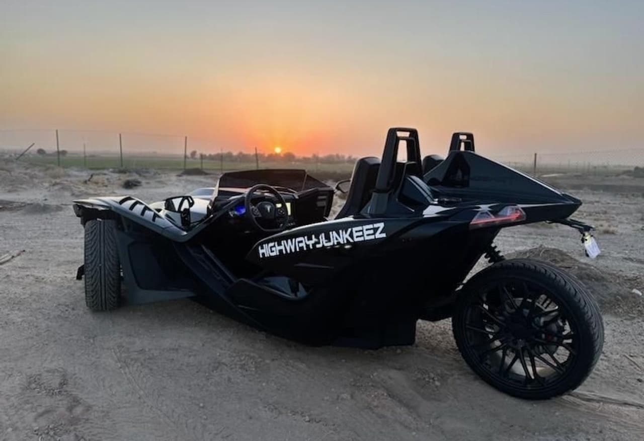 Three-wheeled slingshot on desert dunes at sunset, off-road drive