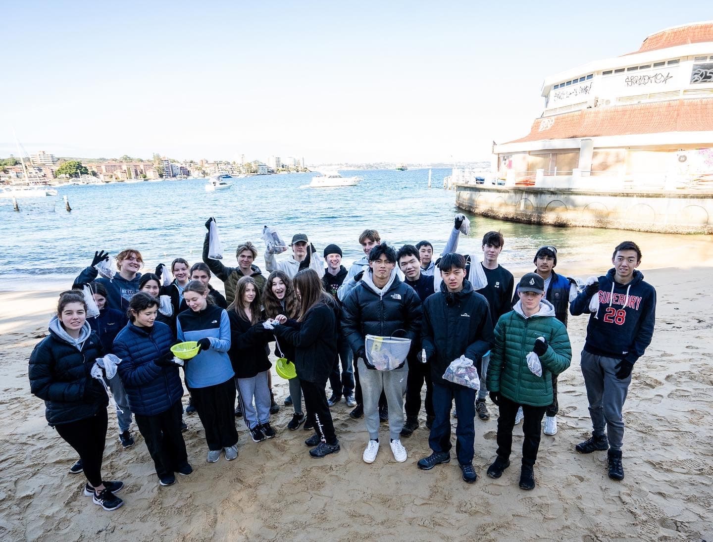 Group beach cleanup volunteers on sandy shore by harbor