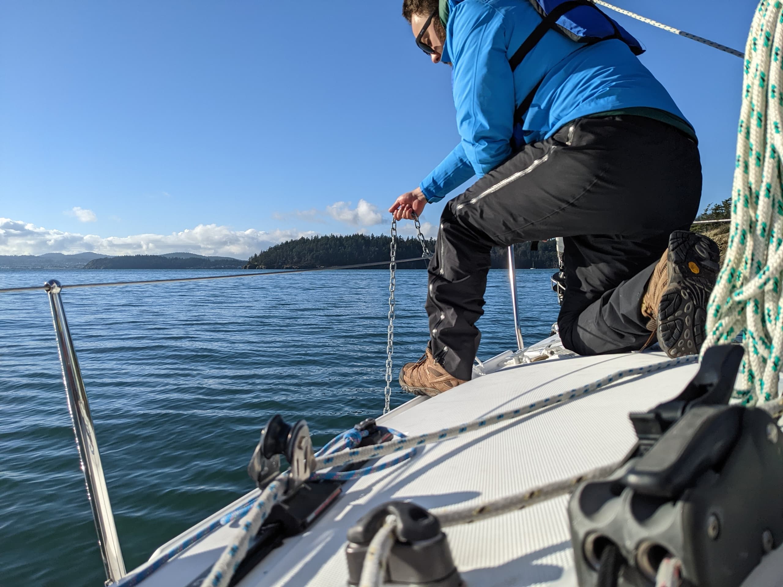 Sailor adjusting rigging on deck with calm sea and island backdrop