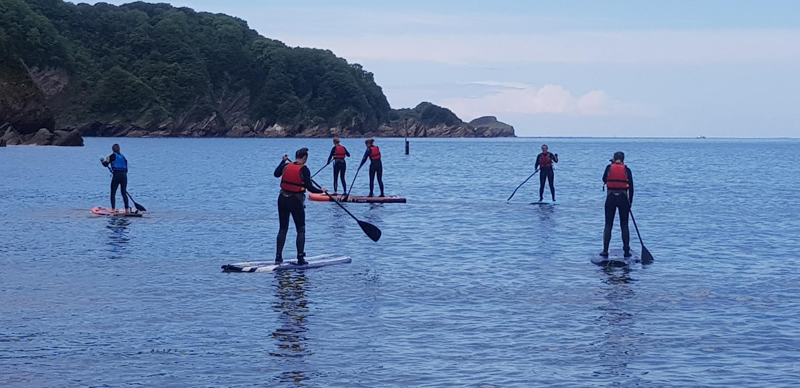 SUP paddlers gliding near coastal headland on calm sea
