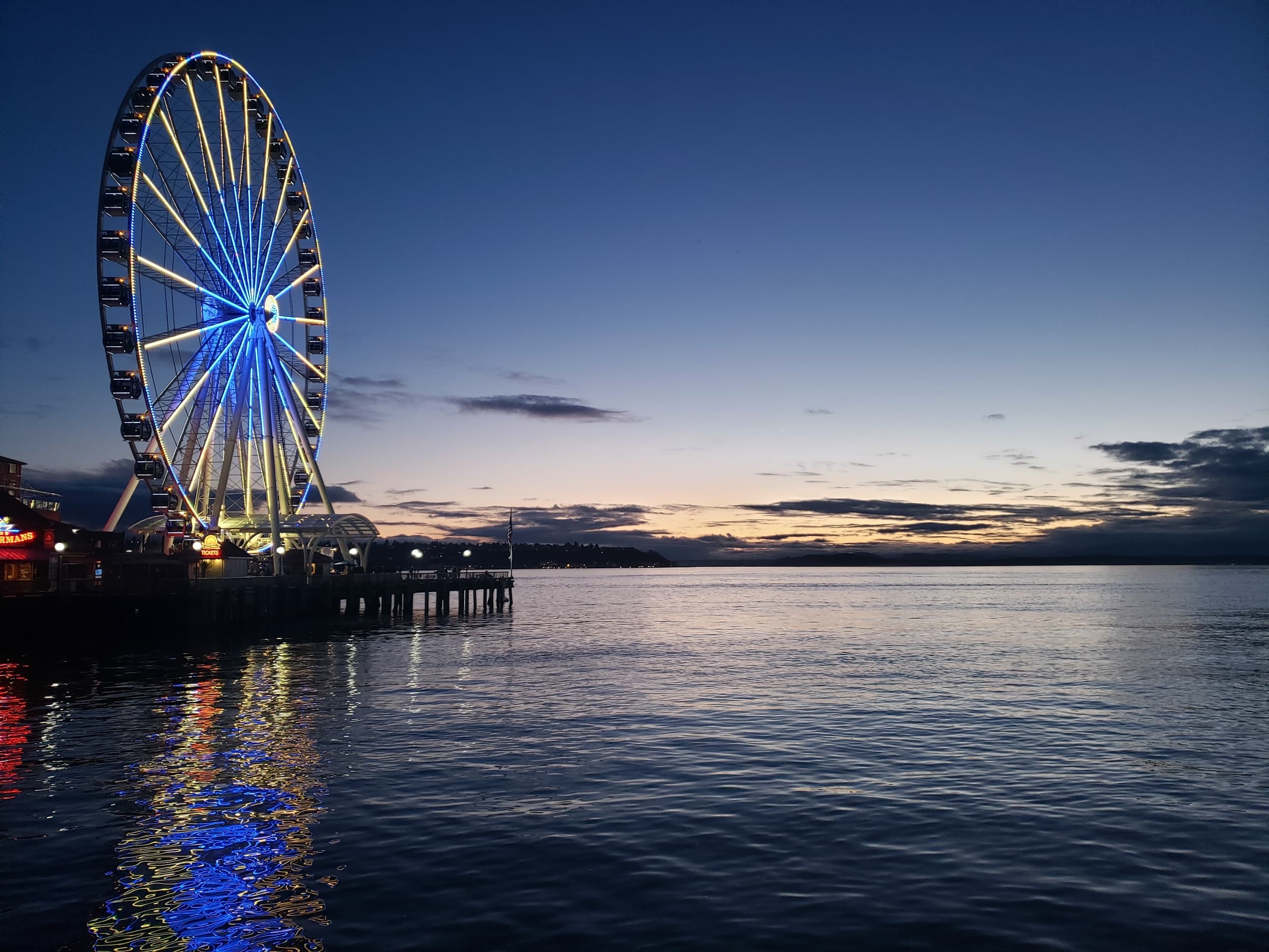 Ferris wheel lit at dusk over calm waterfront with reflections