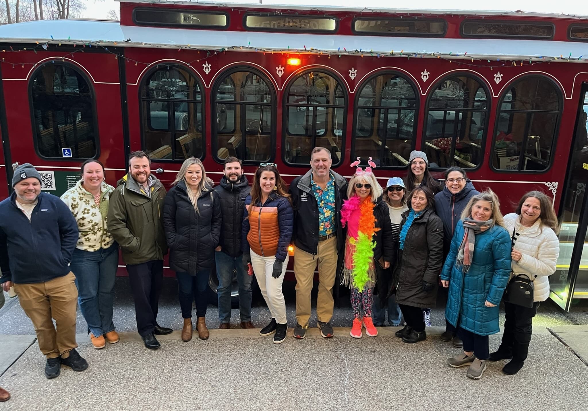 Group of riders posing outside a red trolley during a community tour