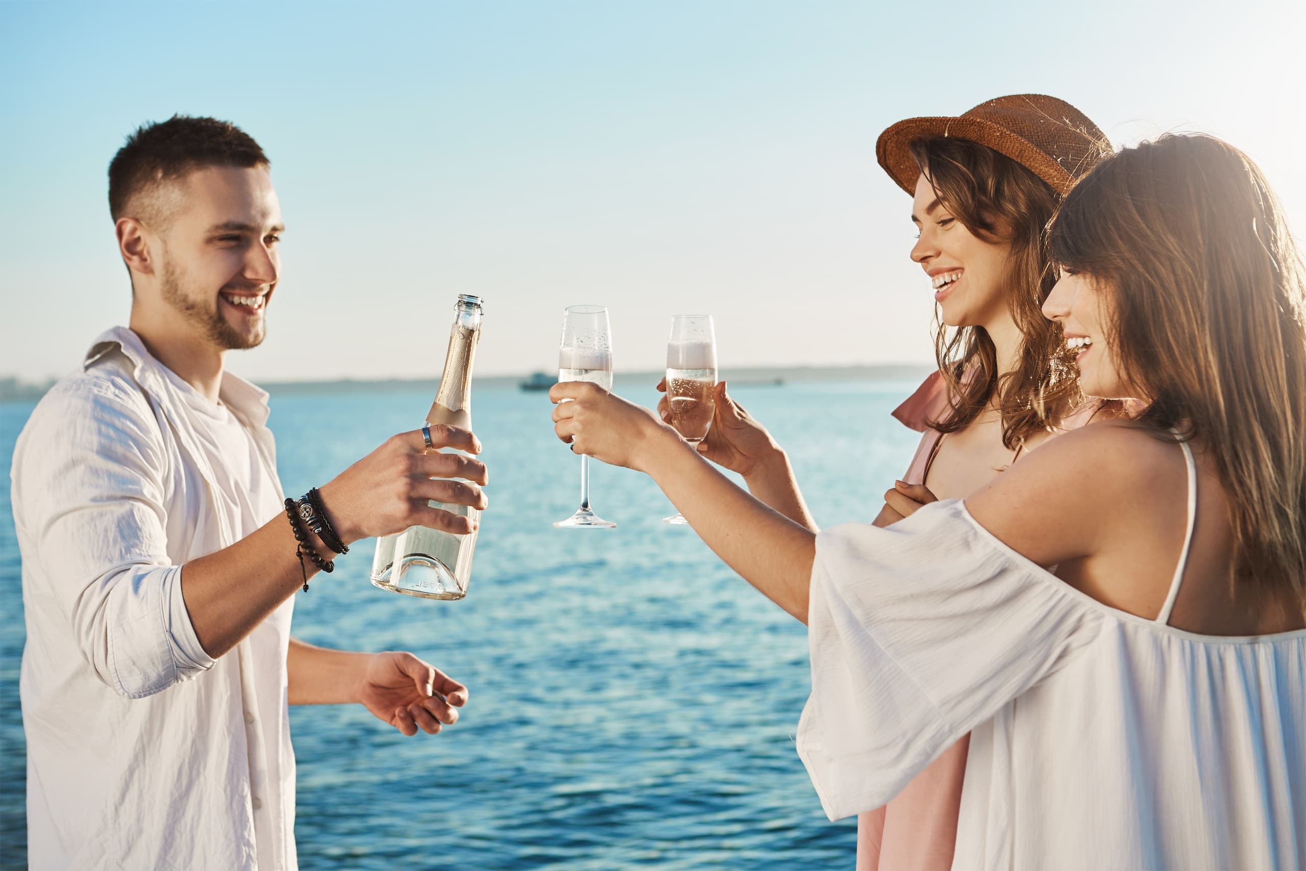 Group toasting with drinks on coastal boat deck during day