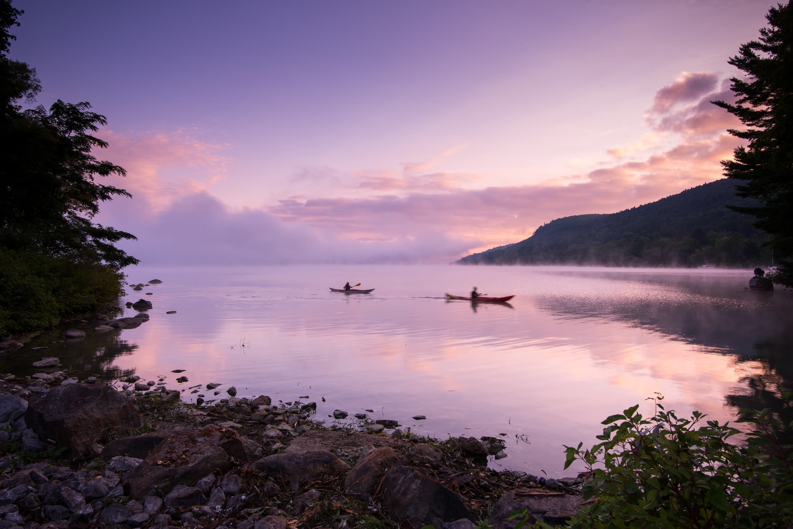 Two kayakers paddling on a misty mountain lake at sunrise
