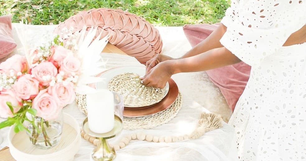 Woman arranging a styled outdoor picnic on grassy park blanket