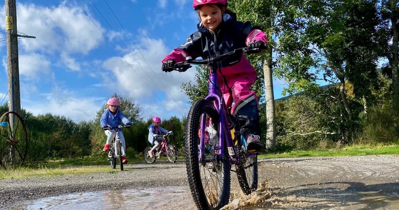 Children mountain biking through muddy country trail with splashes