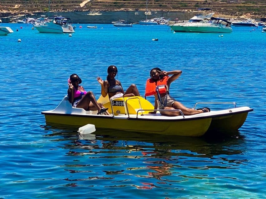 Group on yellow pedal boat enjoying calm blue bay near anchored yachts