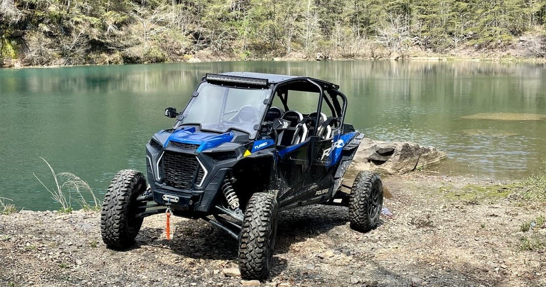 Blue side-by-side UTV parked by forested turquoise lake
